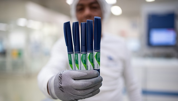 Um homem segura cinco canetas de insulina com a tampa azul e a etiqueta verde